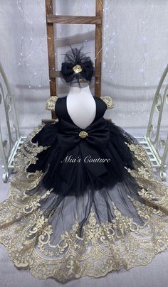 a black and gold dress on display in front of a wooden chair with white lace