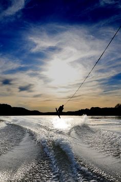 the wake boarder is being pulled through the water by his skis as the sun goes down