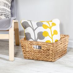 a basket sitting on the floor next to a chair with a pillow and throw pillows in it