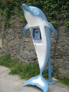 a phone booth shaped like a dolphin is on the sidewalk next to a stone wall