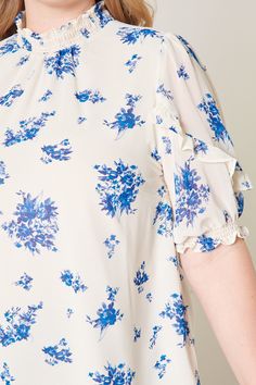 Deep dive in this tonal blue floral blouse that features a high ruffle neck and short puff sleeves. A relaxed fit is maintained throughout the bodice making it perfect for wearing it tucked into a pair of high rise bottoms. Pair it with medium washed denim or make it a set with the matching High Tide Eden Flared Mini Skirt.- Relaxed fit- High neck- Ruffle details- Keyhole- Color: Ivory BlueSize + Fit - Model is 5'10" and wearing size 2X- Measurements taken from size 2X - Chest: 51"- Length: 29" Spring Smocked Top With Short Sleeves And Flowy Fit, Flowy Smocked Top With Short Sleeves For Spring, Feminine Smocked Top With Floral Print And Short Sleeves, Feminine Smocked Top With Floral Print, Feminine Floral Print Smocked Top With Short Sleeves, Spring Short Sleeve Smocked Top, Feminine Short Sleeve Smocked Top With Floral Print, Flowy Smocked Top With Floral Print And Short Sleeves, Casual Floral Smocked Top With Ruffle Sleeves