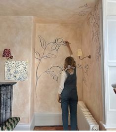 a woman in overalls painting a wall with flowers and leaves on the walls next to a radiator