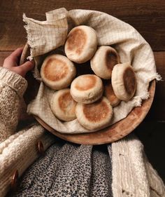 a person holding a wooden bowl filled with small round breads on top of a table