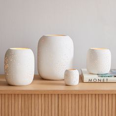 three white ceramic vases sitting on top of a wooden table next to a book