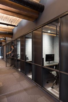 an office with glass partitions and a man standing in the background looking at his computer screen