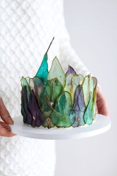 a person holding a cake with green and purple frosting on it's side