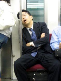 a man sitting on a train with his arms crossed and another person standing next to him