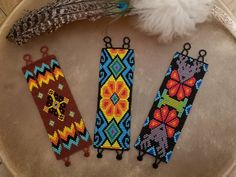 three beaded bookmarks sitting on top of a table next to a white feather