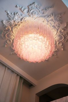 a pink chandelier hanging from the ceiling in a room with white walls and curtains