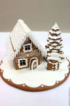 a gingerbread house is decorated with white icing and snow on the roof, along with two trees