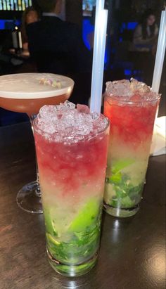 two glasses filled with different colored drinks on top of a wooden table next to each other