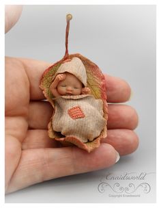 a hand holding a tiny figurine of a baby sleeping in an autumn leaf