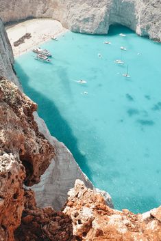 boats are in the blue water near some rocks and cliffs on a sunny day with no one around them