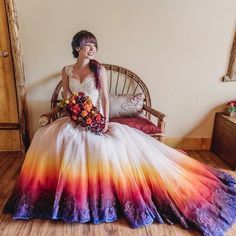 a woman sitting on a chair wearing a colorful dress with flowers in her hair and holding a bouquet