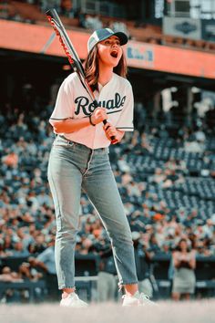 a woman holding a baseball bat in her right hand and looking up at the sky