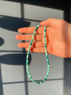 a woman's hand holding a beaded necklace with turquoise beads and green glass beads