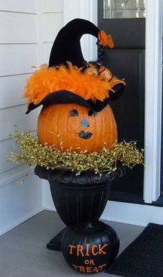 a decorated pumpkin sitting on top of a black pot with orange feathers and a trick or treat written on it