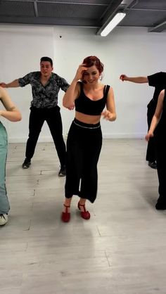 a group of people standing in a room with one person dancing and the other wearing red shoes