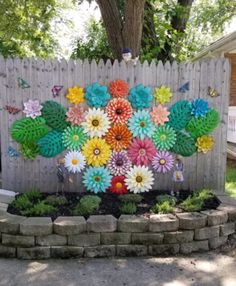 colorful paper flowers are placed on the side of a wooden fence in front of a brick planter