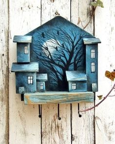 a blue house with a tree and moon painted on the front is mounted to a wooden wall