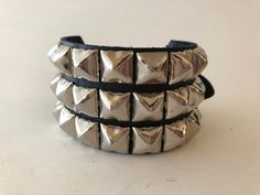 Classic 3 row pyramid stud punk bracelet. Each bracelet is 1.75" wide and has a slight space between each row. Studs are made from nickel plated steel. Buckles made from nickel plated die cast metal alloy, snaps made from nickel plated brass.Buckle bracelets adjust at 1/2" intervals for custom fit. Bracelets also available with snaps. Larger snap bracelets will have more studs per row.Please note: the 7-7.75" bracelet has snaps. These are measured snap to snap so for comfort order something 1/2 Pyramid Bracelet, Studded Bracelet, Classic Punk, 1980s Style, Gothic Bracelet, Snap Bracelets, Buckle Bracelet, Wide Bracelet, Rock Punk