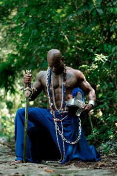 a man sitting on the ground with chains around his neck and holding a cup in one hand