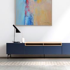 an abstract painting hangs on the wall above a blue cabinet with drawers and a lamp