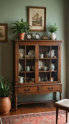 a wooden cabinet filled with lots of dishes next to a chair and potted plant