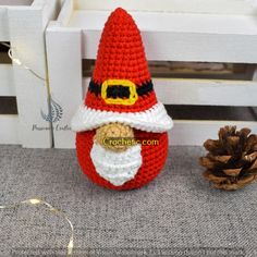 a crocheted santa claus ornament next to a pine cone