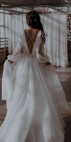 the back of a woman in a white dress with long sleeves and flowing fabric on it