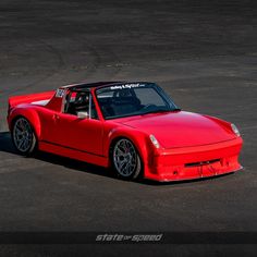 a red sports car parked in a parking lot next to a black tarmac area