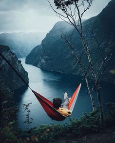 a person laying in a hammock on the edge of a cliff overlooking a body of water