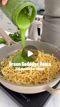 someone pouring green liquid over noodles in a pan