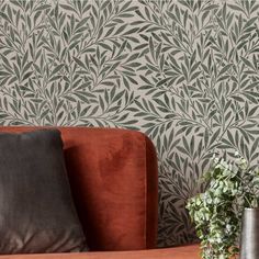 a red couch sitting in front of a wallpapered with leaves and plants on it