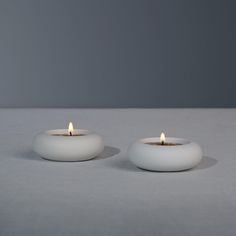 two white candles sitting next to each other on top of a gray tablecloth covered surface