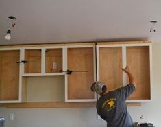 a man working on cabinets in a kitchen with white walls and wood trimmings