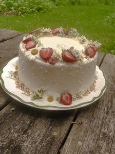 a white cake with strawberries and daisies on top sitting on a wooden table