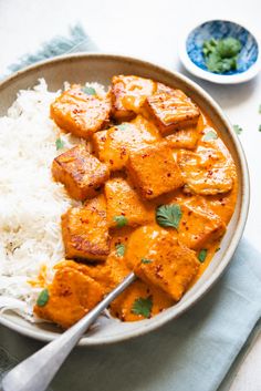 a bowl filled with rice and tofu on top of a white table next to a spoon