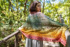 a woman standing on a bridge wearing a colorful crocheted shawl