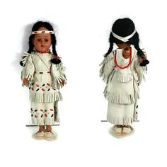 two dolls dressed in native american clothing, one with black hair and the other white