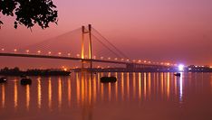 the bridge is lit up at night with lights reflecting in the water and boats on the river below