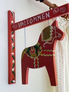 a wooden sign hanging from the side of a white wall next to a red horse