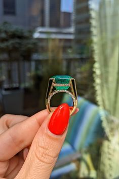 a woman's hand holding a ring with an emerald and diamond set in it