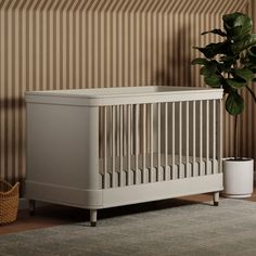 a white crib next to a potted plant on the floor in front of a striped wall