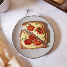 two slices of toast with tomatoes and cheese on them next to a cup of coffee