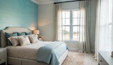 a bedroom with blue walls and white bedding in front of a large window that has curtains