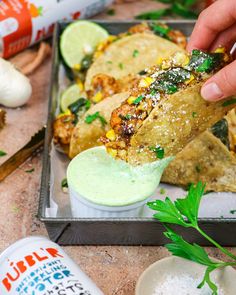 a person dipping sauce on some food in a container with other ingredients around the tray