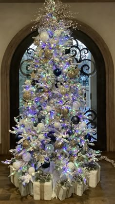 a white christmas tree with blue and silver ornaments in front of a arched window at night