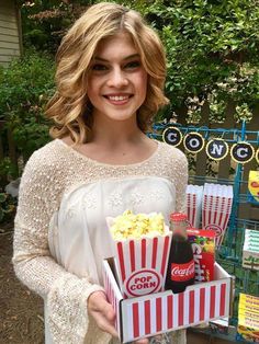 a woman holding a box of popcorn and soda