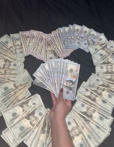 a hand reaching for money on top of a black cloth covered table with lots of twenty dollar bills